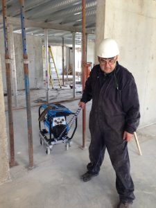 Welder pulls a small portable and self-propelled welding machine on construction site of condominium building. By JW Portable Welding & Repair, London, Ontario, 2020